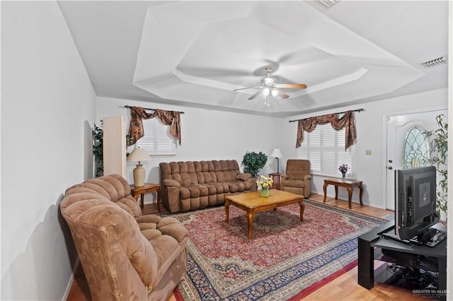 living room with wood-type flooring, a tray ceiling, and ceiling fan