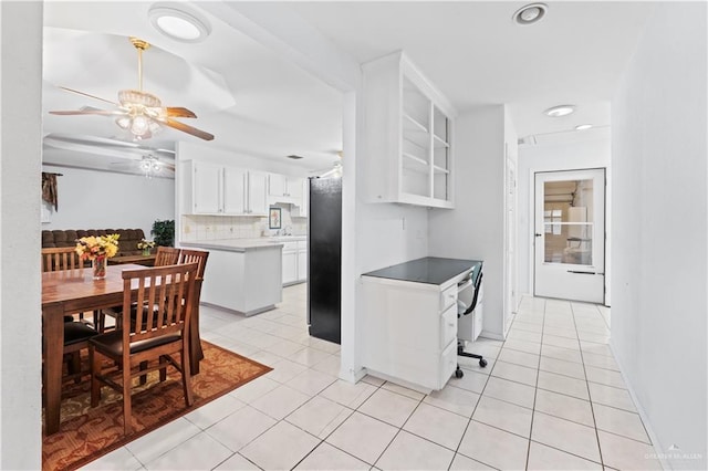 kitchen featuring black refrigerator, light tile patterned flooring, white cabinetry, and backsplash