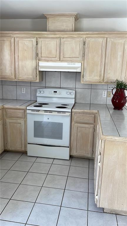 kitchen with light brown cabinetry, backsplash, electric stove, light tile patterned floors, and tile counters