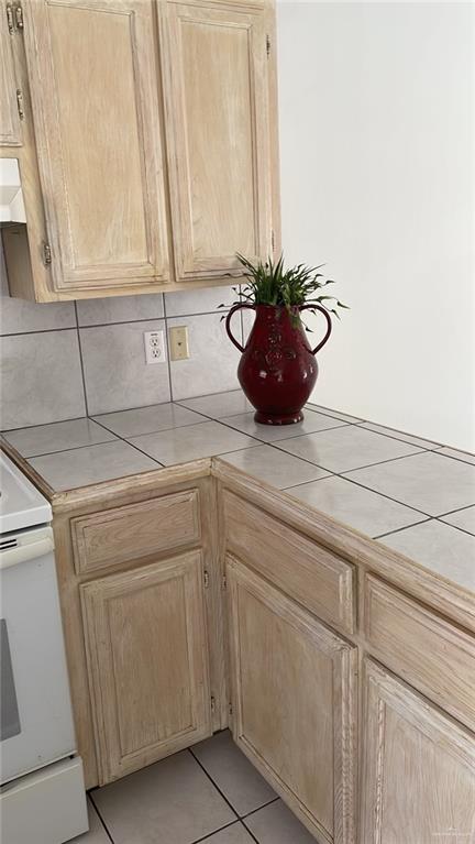 kitchen featuring light brown cabinets, tasteful backsplash, white electric stove, and tile counters