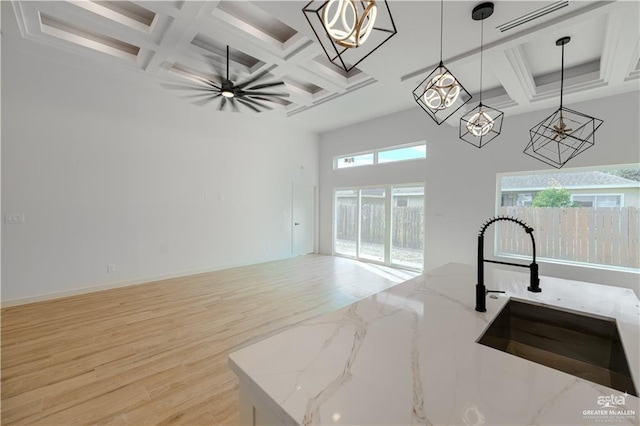 kitchen with coffered ceiling, a towering ceiling, decorative light fixtures, light stone countertops, and light wood-style floors