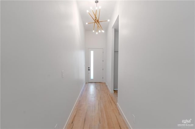 hallway with light wood-type flooring, a high ceiling, baseboards, and a notable chandelier