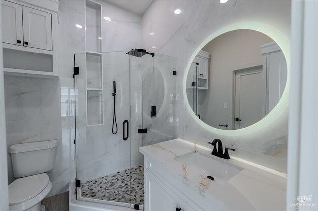 bathroom featuring toilet, tile walls, a marble finish shower, and vanity