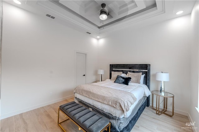 bedroom with light wood-style floors, a tray ceiling, visible vents, and baseboards