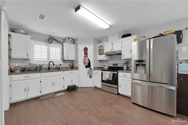 kitchen with white cabinets, dark stone countertops, stainless steel appliances, and hardwood / wood-style floors