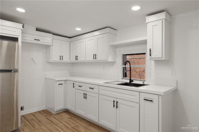 kitchen featuring stainless steel refrigerator, white cabinetry, and sink