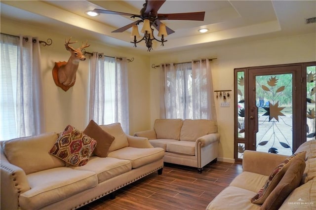 living room with a raised ceiling, ceiling fan, and dark wood-type flooring