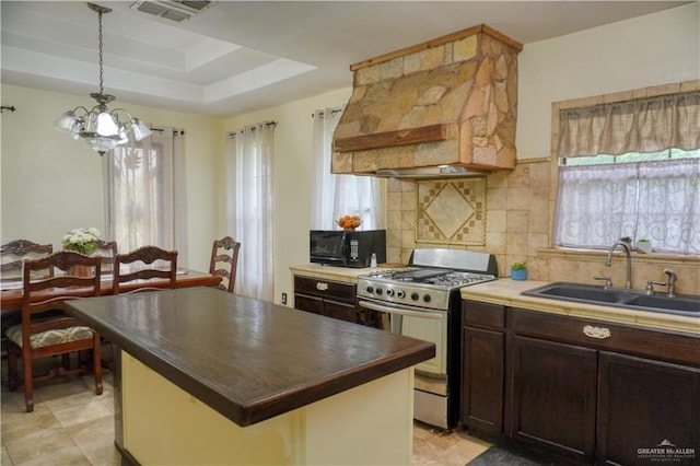 kitchen with custom range hood, pendant lighting, stainless steel range with gas cooktop, a tray ceiling, and sink