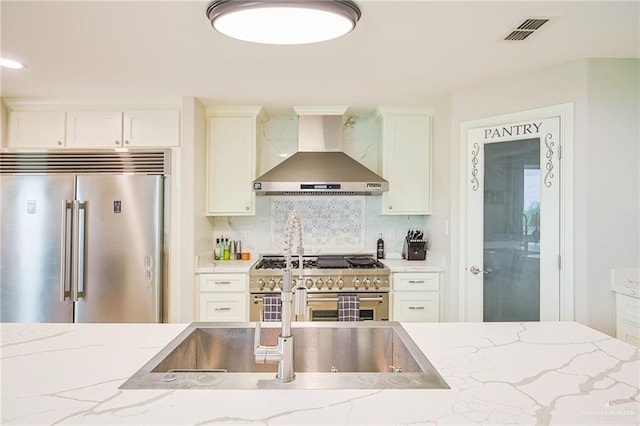 kitchen featuring light stone countertops, wall chimney exhaust hood, backsplash, high quality appliances, and white cabinets