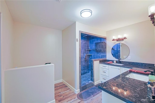 bathroom with a tile shower, vanity, and wood-type flooring