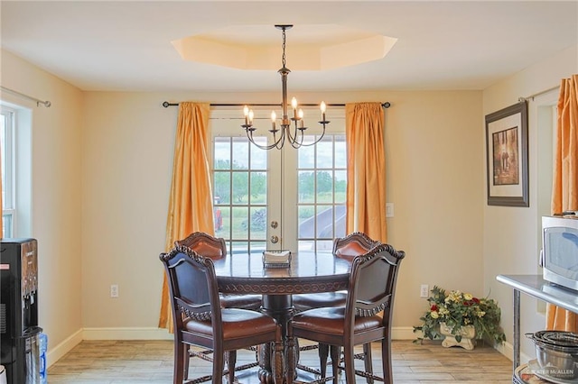 dining space featuring light hardwood / wood-style floors, a raised ceiling, french doors, and a chandelier