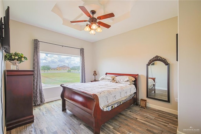 bedroom featuring a raised ceiling, ceiling fan, and dark wood-type flooring