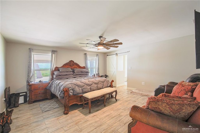 bedroom with multiple windows, ceiling fan, light hardwood / wood-style flooring, and a barn door