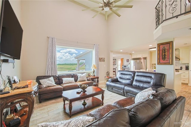 living room with ceiling fan, light hardwood / wood-style floors, and a high ceiling