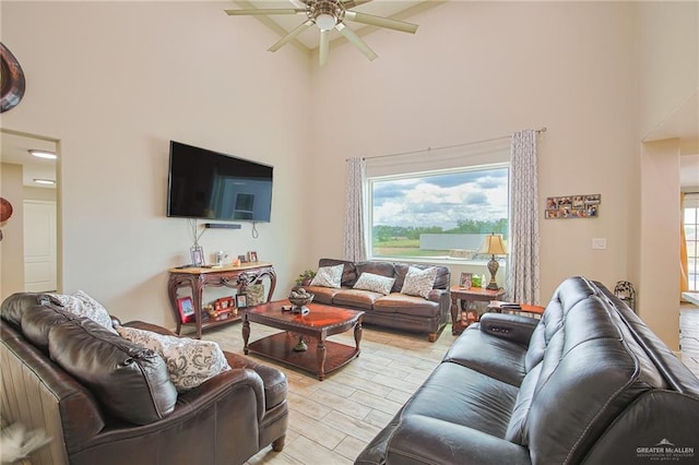 living room with a high ceiling, light wood-type flooring, and ceiling fan