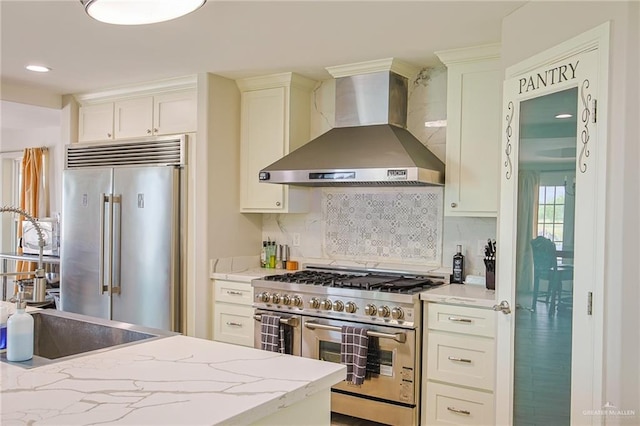 kitchen featuring decorative backsplash, premium appliances, light stone counters, and wall chimney range hood