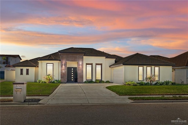 prairie-style house with a garage, driveway, a front yard, and stucco siding