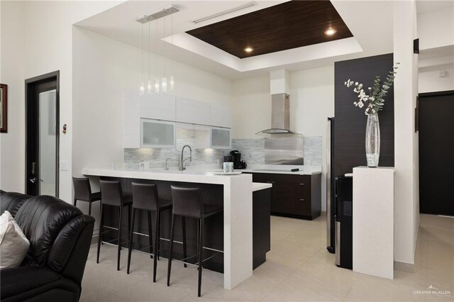 kitchen with a peninsula, a breakfast bar, light countertops, modern cabinets, and a raised ceiling