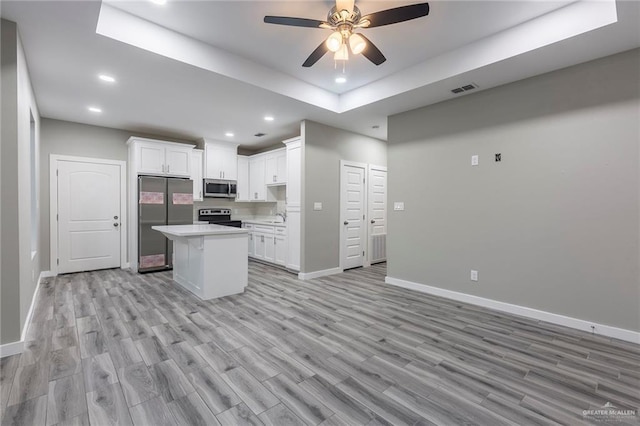 kitchen featuring a kitchen island, white cabinetry, stainless steel appliances, a raised ceiling, and light hardwood / wood-style flooring