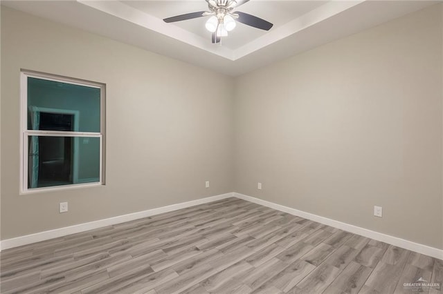 unfurnished room featuring a raised ceiling, ceiling fan, and light hardwood / wood-style flooring