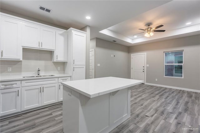 kitchen with ceiling fan, white cabinets, a tray ceiling, and sink