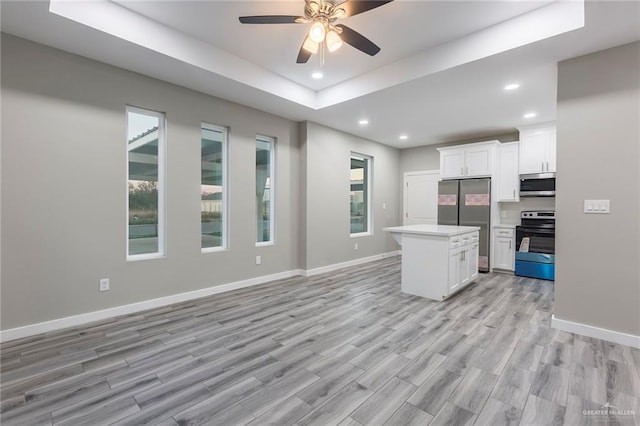 kitchen with a raised ceiling, appliances with stainless steel finishes, white cabinetry, and a center island