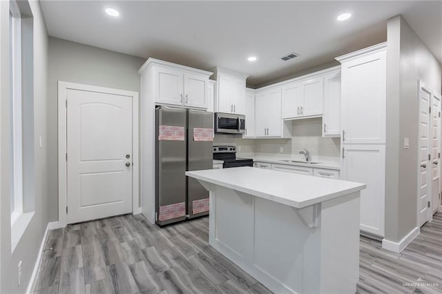 kitchen featuring appliances with stainless steel finishes, a center island, white cabinets, light hardwood / wood-style flooring, and sink