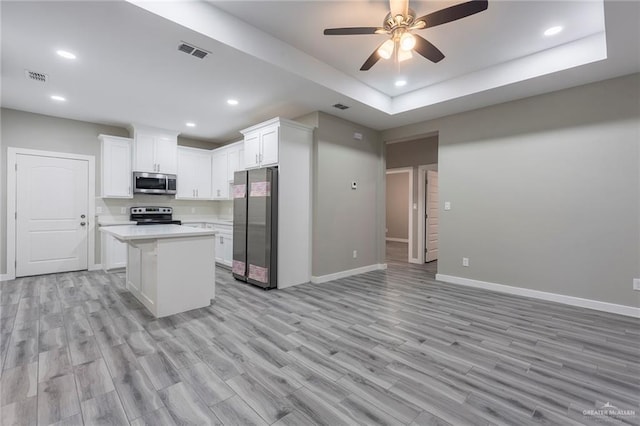 kitchen with white cabinets, appliances with stainless steel finishes, a center island, a raised ceiling, and light hardwood / wood-style flooring