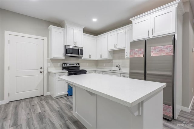 kitchen with appliances with stainless steel finishes, a center island, white cabinetry, light hardwood / wood-style floors, and sink