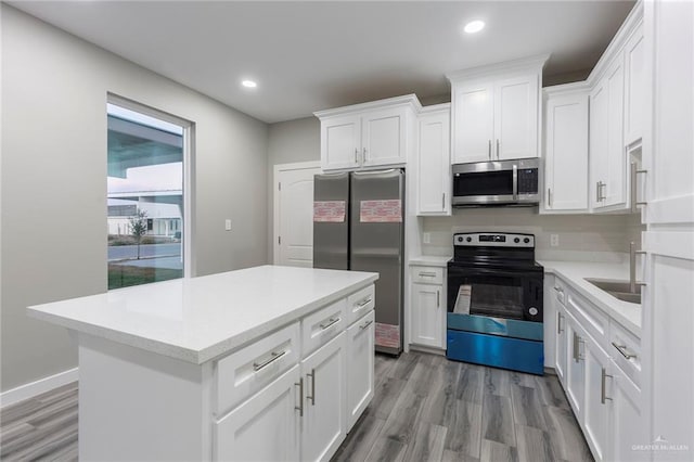 kitchen with appliances with stainless steel finishes, a kitchen island, white cabinetry, and light hardwood / wood-style flooring