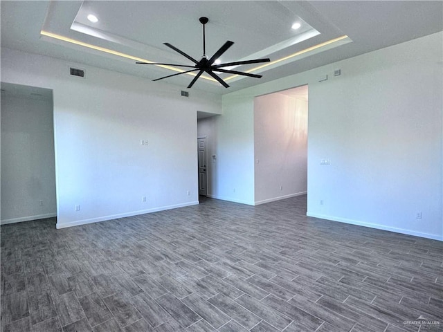 spare room with visible vents, baseboards, ceiling fan, dark wood-style floors, and a tray ceiling