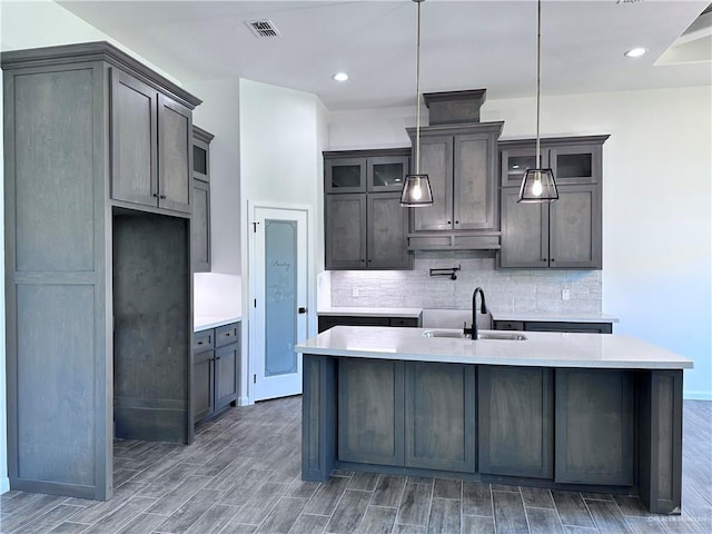 kitchen featuring a sink, light countertops, wood finished floors, backsplash, and a center island with sink