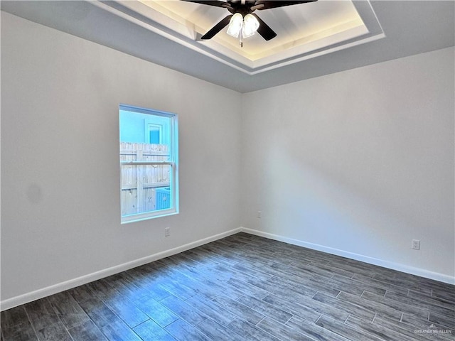 empty room featuring a raised ceiling, ceiling fan, baseboards, and dark wood-style flooring