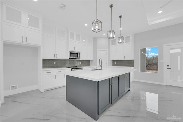 kitchen with tasteful backsplash, white cabinets, hanging light fixtures, stainless steel appliances, and a center island with sink