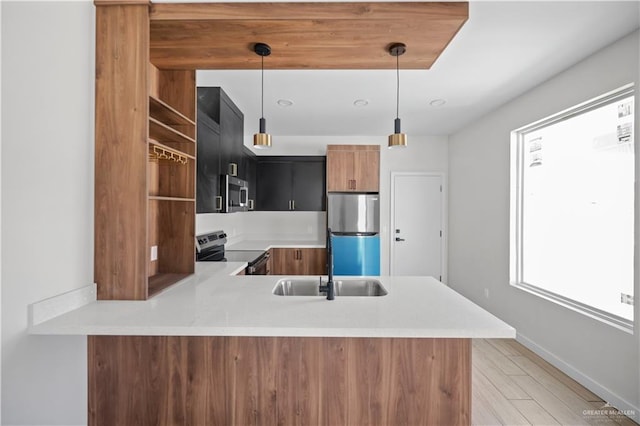 kitchen featuring decorative light fixtures, stainless steel appliances, light countertops, a sink, and a peninsula