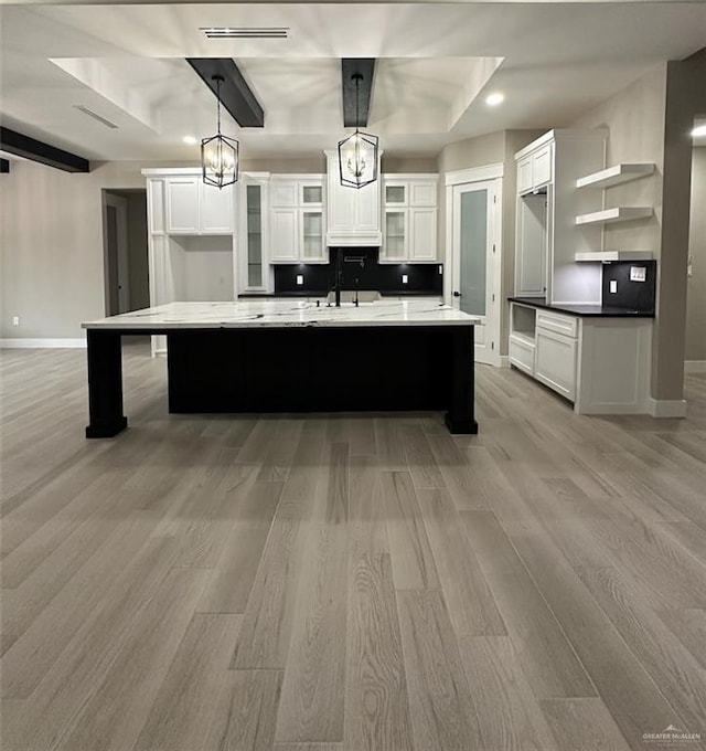 kitchen featuring backsplash, white cabinets, hanging light fixtures, an island with sink, and light hardwood / wood-style floors