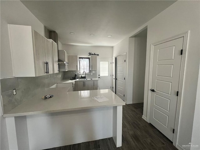 kitchen with backsplash, kitchen peninsula, dark hardwood / wood-style flooring, and sink