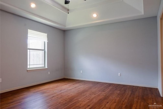 empty room with a raised ceiling, ceiling fan, and wood-type flooring