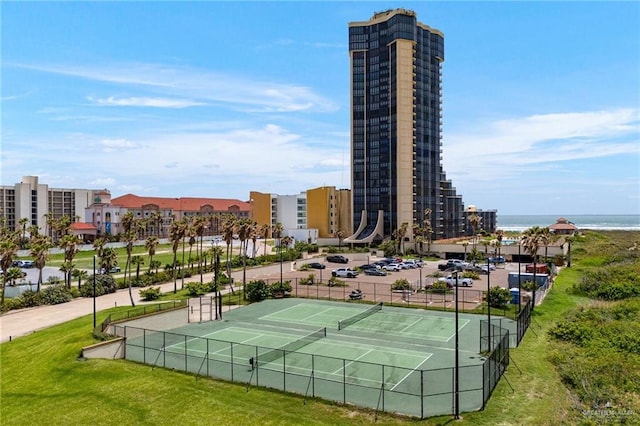 view of tennis court featuring a city view, fence, and a water view