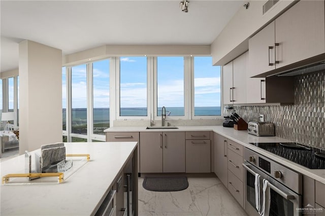 kitchen featuring marble finish floor, black electric stovetop, a sink, and a water view