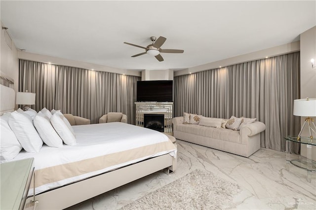 bedroom featuring a tiled fireplace, marble finish floor, and ceiling fan