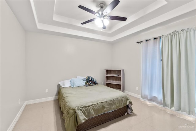 tiled bedroom with a ceiling fan, a raised ceiling, and baseboards