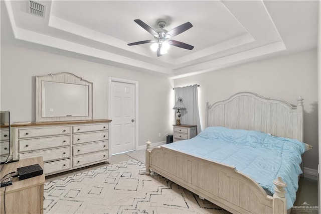 bedroom featuring baseboards, ceiling fan, visible vents, a raised ceiling, and light carpet