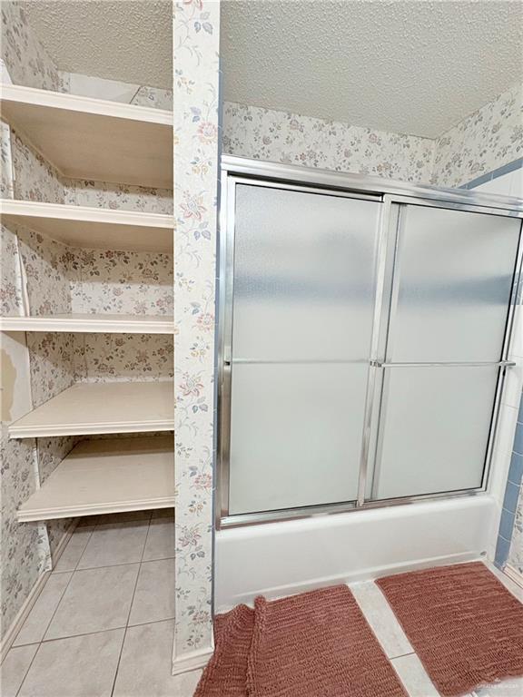 2218 Lawndale Rd, Mission, TX 78572 - full bathroom featuring a textured ceiling, wallpapered walls, bath / shower combo with glass door, baseboards, and tile patterned flooring