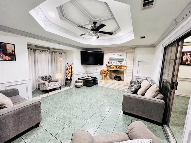 living room featuring ceiling fan, ornamental molding, a fireplace, a tray ceiling, and light tile patterned flooring