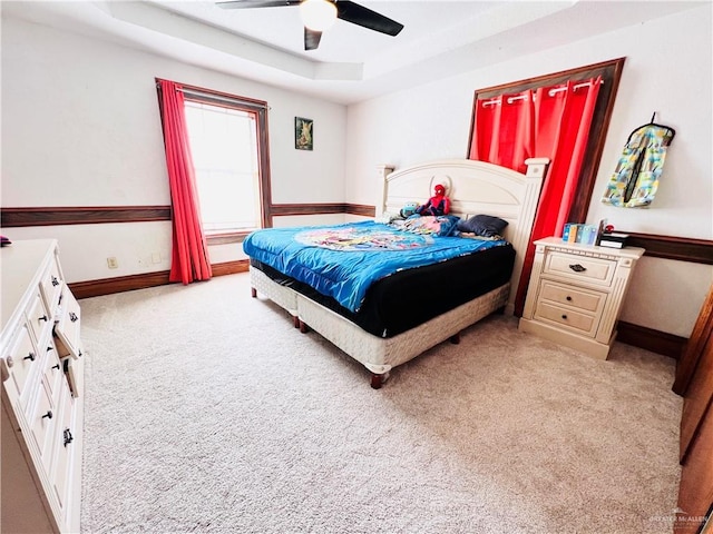 bedroom featuring light carpet, a tray ceiling, and ceiling fan