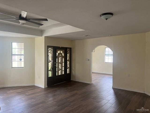 entrance foyer with arched walkways, dark wood-style flooring, and baseboards