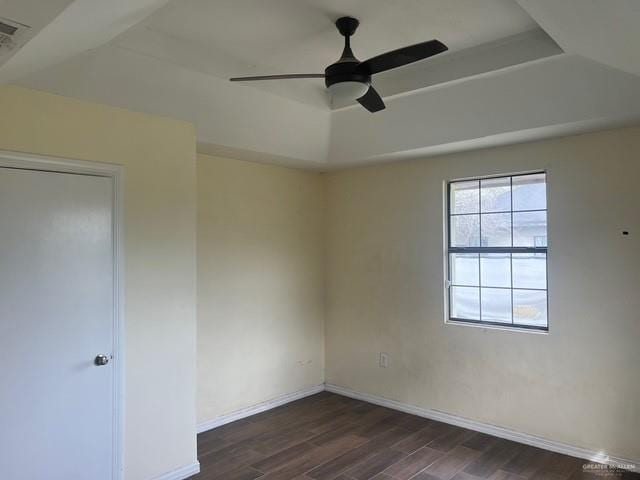 unfurnished room featuring a tray ceiling, dark wood-type flooring, a ceiling fan, and baseboards