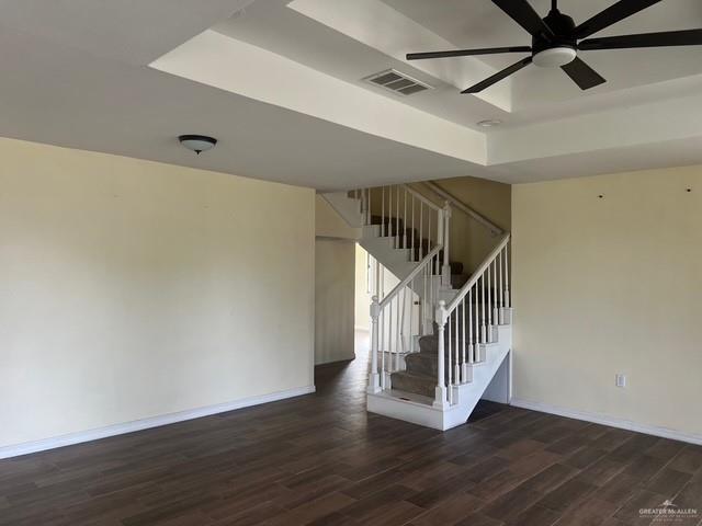 spare room featuring dark wood-style floors, stairway, a raised ceiling, and baseboards