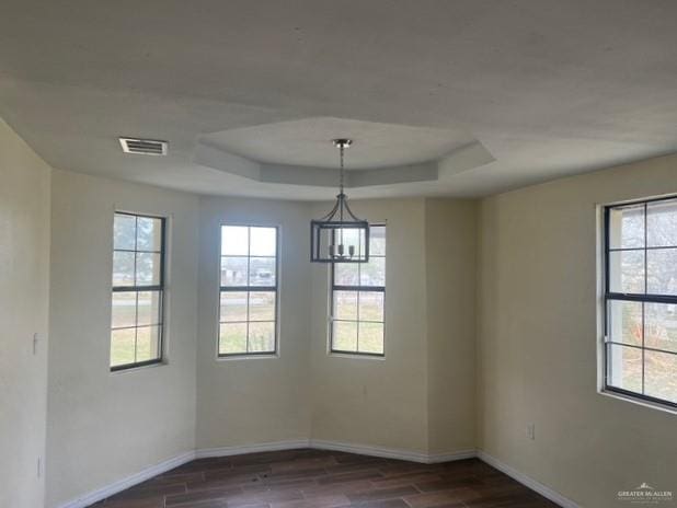 unfurnished dining area featuring dark wood-type flooring, a raised ceiling, and a wealth of natural light